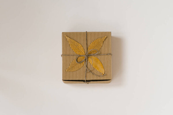 craft gift box, tied with string with a bow and autumn fallen leaves on a beige background. Birthday gift for people born in autumn. Top view