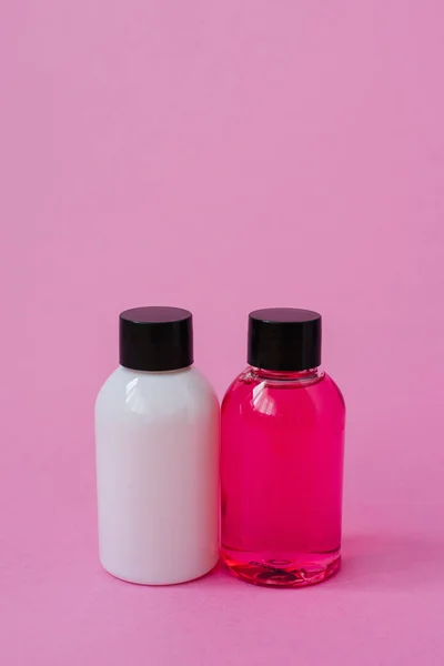 Shower gel and shampoo in a small rounded bottle with a black cap on a pink background.
