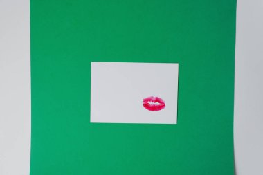 Dudak baskılı beyaz kart, yeşil ve beyaz arka plan üzerinde beyaz kağıt üzerinde ruj. Kopya alanı. Mektupta bir öpücük