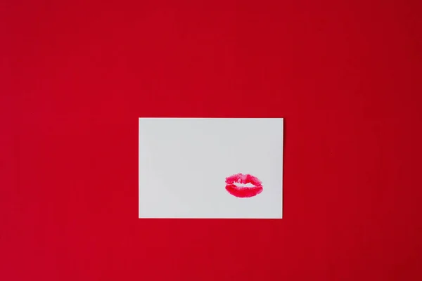Red lipstick lip print Kiss on white paper sheet on red background