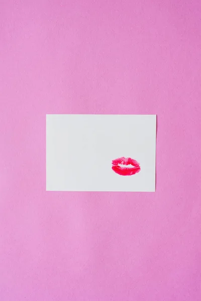 Red lipstick lip print Kiss on white paper sheet on pink background