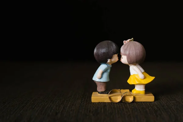 A statuette of a guy and a girl kissing and gold wedding rings on a brown background