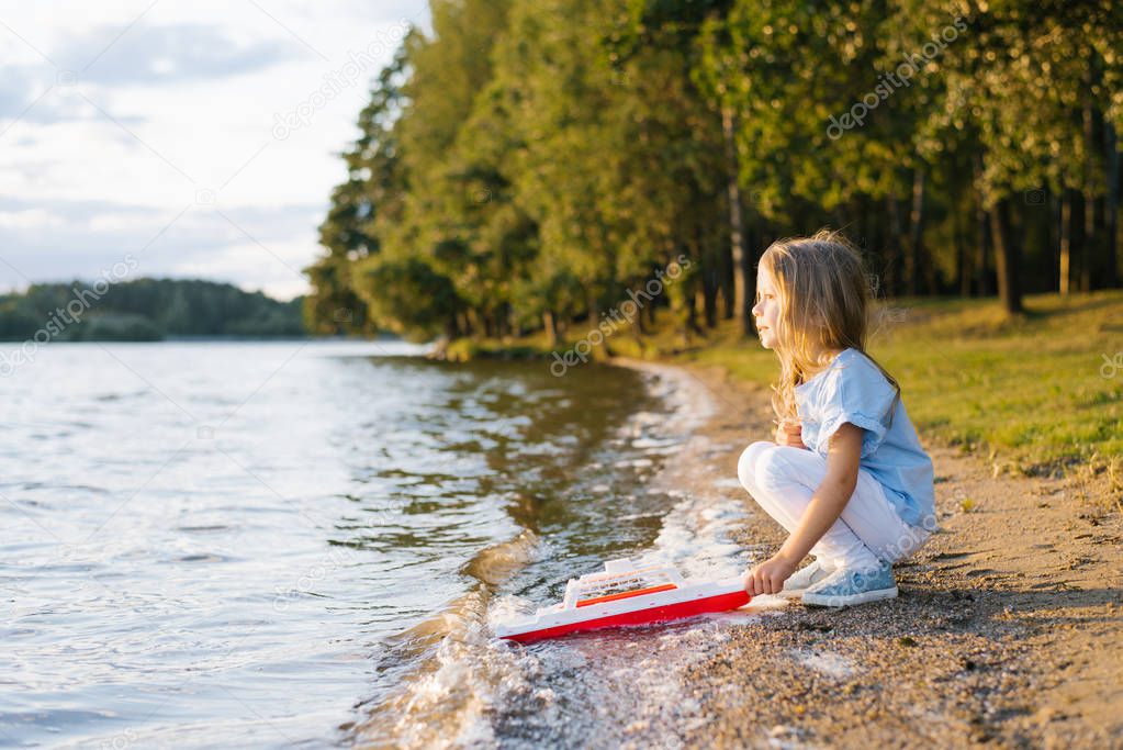 Child girl holding a toy ship and launches it into the water of the lake