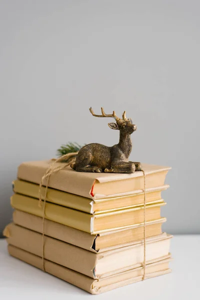 A stack of books in a craft cover, tied with twine, on the books is a statuette of a sitting deer on a gray background