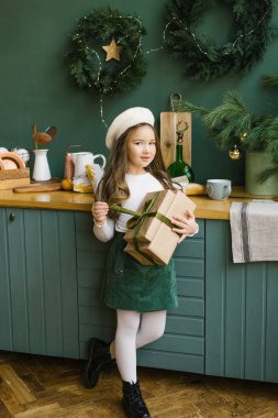 Beş ya da altı yıllık şık bir kız yeni yıl için süslenmiş bir Noel hediyesini mutfakta tutuyor.