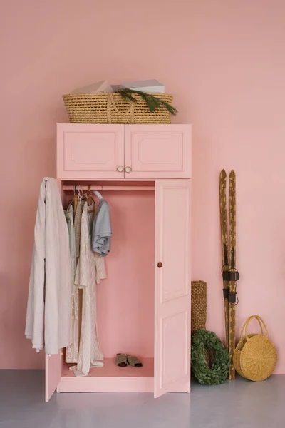 Wardrobe with clothes, wooden retro skis and Christmas wreath in pink living room