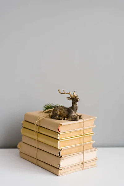 A pile of books in craft covers, tied with twine, on which stands a statuette of a Christmas deer. Copy space