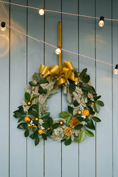 A Christmas tree wreath hangs on a dusty blue wooden wall