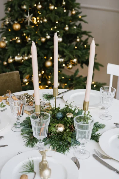美しいガラスグラス お祝いのテーブルの装飾でキャンドル クリスマスツリーを背景にしたクリスマステーブルの設定 — ストック写真