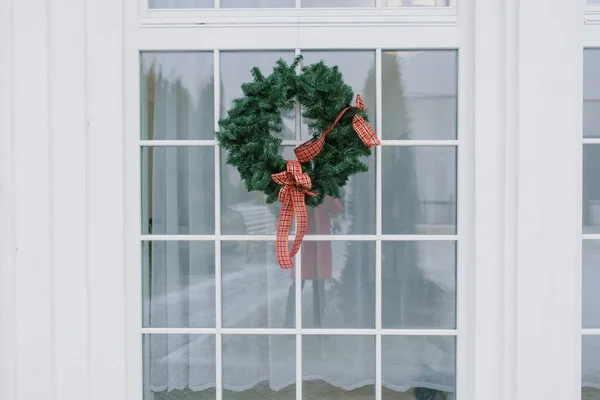 Christmas wreath with a red bow on a white window in a private house