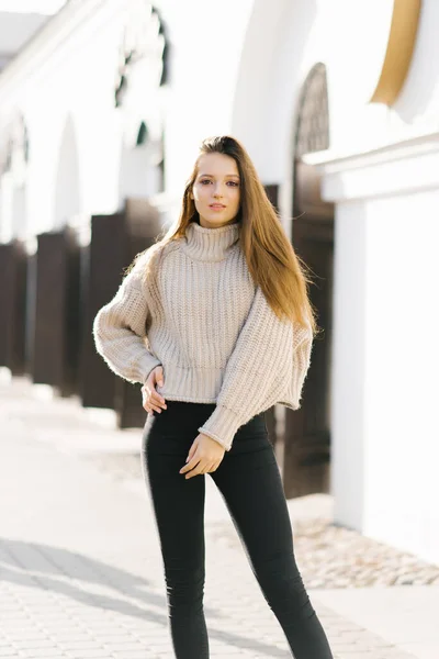ニットのセーターと黒いジーンズを着たかなりファッショナブルな若い女性が街の通りに沿って散歩を楽しんでいます 魅力的な女の子でファッショナブルな服で街 — ストック写真