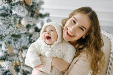 Mutlu bir anne ve Noel 'i kutlayan sevimli bir çocuğun portresi. Noel ağacı ve süslemelerle süslenmiş bir odada annenle gülümseyen bebek..