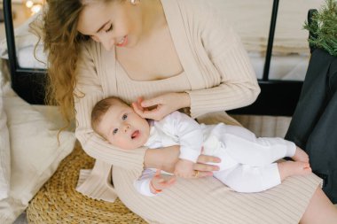 Noel ağacının yanında güzel bir çocukla gülümseyen bir annenin portresi. Annem yerde oturup bebeğe sarılıyor. Arka planda Noel dekorlu bir yatak var. .