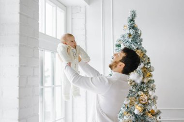 Genç bir baba onu kollarına aldı ve evdeki Noel ağacının yanında kaldırdı.