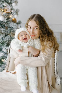 Mutlu bir anne ve Noel 'i kutlayan sevimli bir çocuğun portresi. Yeni yıl tatili. Noel ağacı ve süslemeleri olan bir odada annenle bebek..