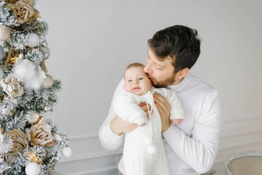 Babam, parlak oturma odasındaki Noel ağacının yanında küçük bir çocuğu yanağından öpüyor. Ailede yeni yıl kutlaması
