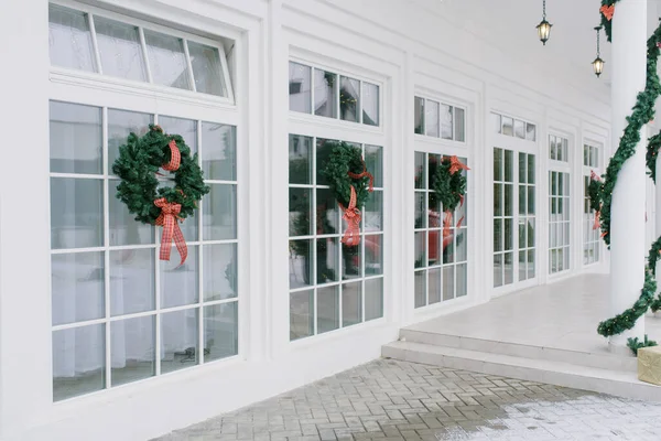 Christmas decorations: wreaths with bows on the white French Windows of a private home