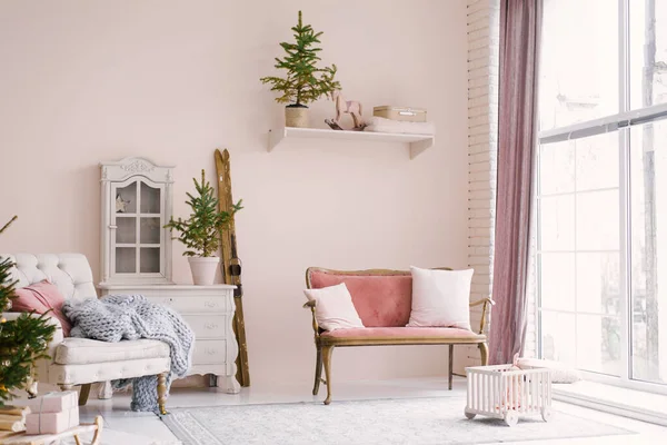 A pink vintage sofa with pillows stands near the window in the living room or children's room, decorated for Christmas or New Year, in the house. Minimalistic interior design