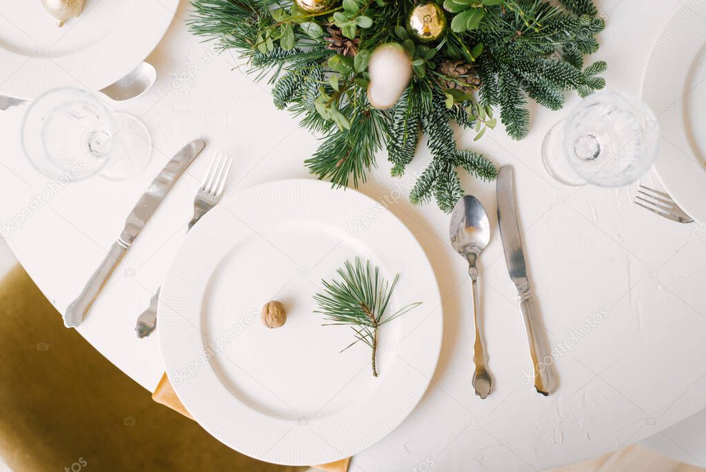 Christmas table setting with white plates, silver Cutlery, Christmas wreath on a white table. Christmas dinner, party design, concept.
