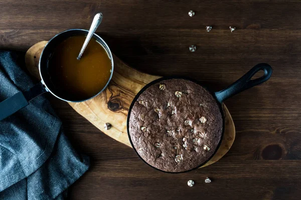 Küçük bir tavada pişmiş çikolatalı brownie 'nin üstten görünüşü ve üzerine yayılacak küçük bir tencere sıcak karamel sosu..