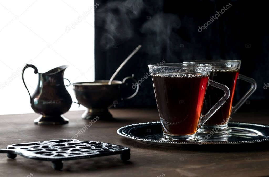 A close up of two steaming cups of tea ready for drinking against a black background.