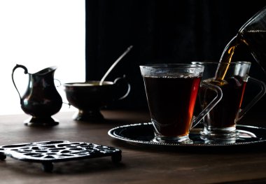 Bir fincana çay, arkaya da antika krema ve şeker kalıpları dökülen iki fincan çayın yakın görüntüsü..