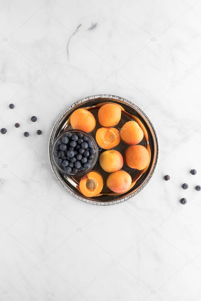 A top down view of apricots and a small bowl of blueberries on a metal tray. A complimentary colour concept.