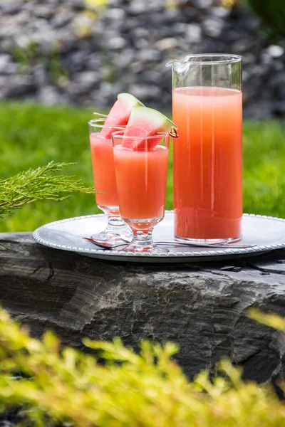 Guava juice garnished with watermelon wedges on a metal tray resting on a rock outside. — Stock Photo, Image