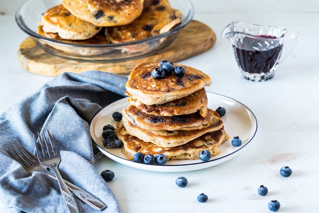 Blueberry pancakes stacked on a plate with blueberry syrup, ready for eating.