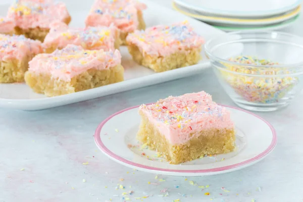 Low carb Keto sugar cookie bar on a small plate with a platter of them in behind.