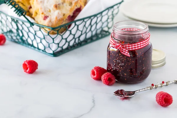 A jar of raspberry jam with a basket of scones in behind. — Stock Photo, Image