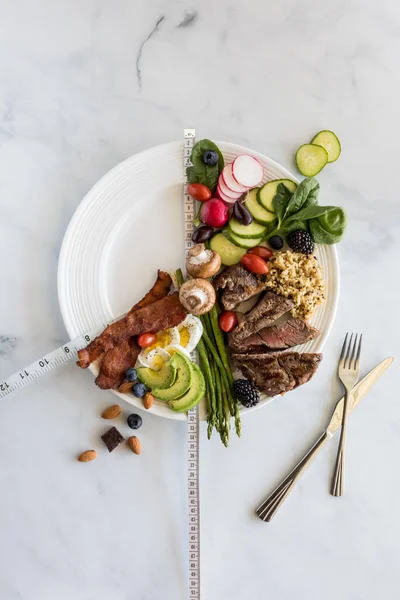 Digiuno intermittente concetto di perdita di peso. Vari alimenti a basso contenuto di carboidrati su un piatto bianco su uno sfondo di marmo bianco. — Foto Stock
