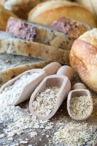 Close up de colheres de madeira cheias de farinha, aveia e farelo de aveia e rodeado de pão. — Fotografia de Stock