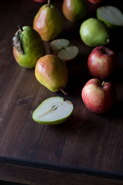 Gros plan des poires et des pommes sur une table en bois sombre et éclairée du côté. — Photo