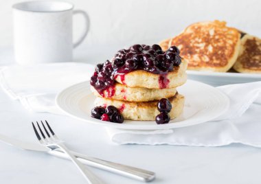 Üstünde sıcak yaban mersini sosu ve daha fazla krep olan taze bir krep yığını..
