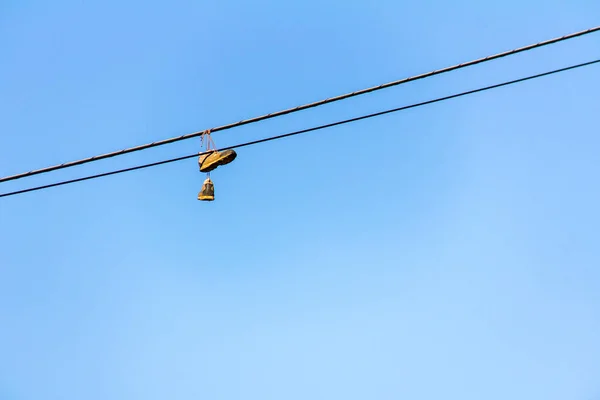 Gamla sneakers hängande på elektrisk tråd med blå himmel i bakgrunden på en solig dag — Stockfoto