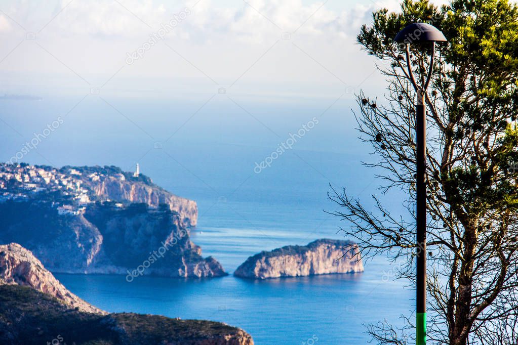 Panoramic view of La Nao cape in Javea, Spain. A tree and a streetlamp in the foreground. View from Cumbre del Sol Mountain, also known as 