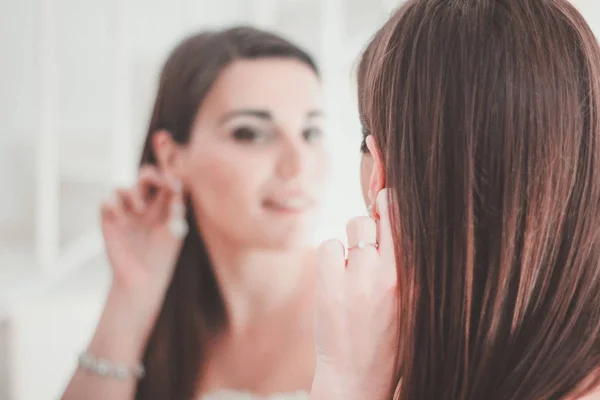 Young bride at the mirror with an earring