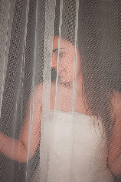 Portrait of a young bride posing behind a curtain — Stock Photo, Image