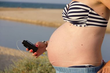 A diabetic pregnant woman with an insulin pump on the beach. She clipart