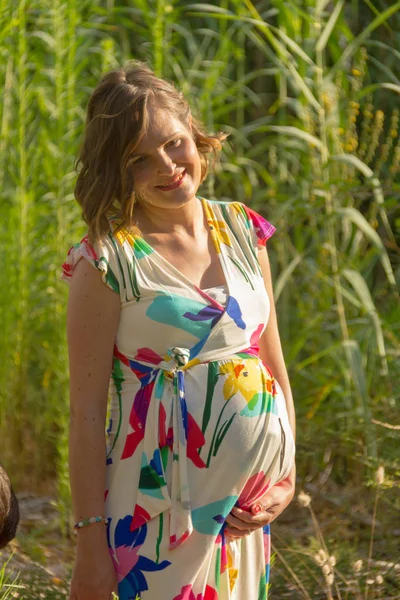 Eine junge schwangere Frau mit einem bunten Kleid posiert in einem Park — Stockfoto