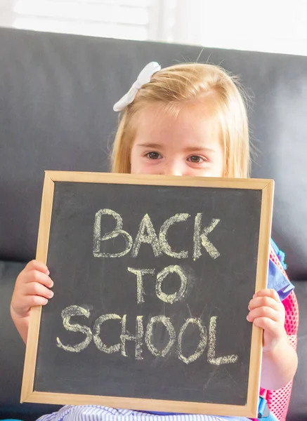 Back to school. A cute blonde little girl showing a chalkboard with \