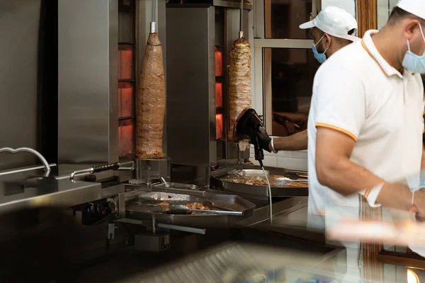 Üniformalı bir aşçı, fast food standında tavuk ve sığır kebabı kesiyor ve hazırlıyor.