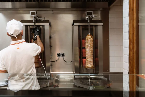 Üniformalı bir aşçı, fast food standında tavuk ve sığır kebabı kesiyor ve hazırlıyor.