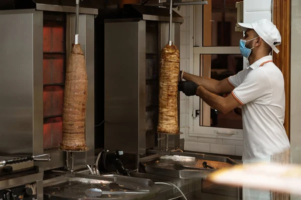 Üniformalı bir aşçı, fast food standında tavuk ve sığır kebabı kesiyor ve hazırlıyor.