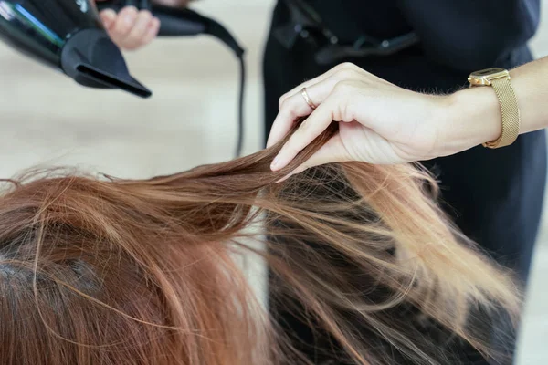 Elegant young hairdresser with face mask drying her client\'s hair in a modern hairdressing salon . Social distancing. Close-up