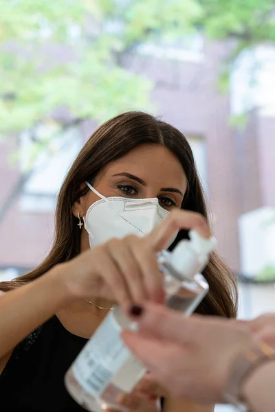 顔のマスクで保護された若いお店のアシスタントは 手の細菌に対する衛生のために顧客にアルコールジェルを分配します 感染の予防 新常態 ロイヤリティフリーのストック画像