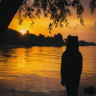 Romantik bir deniz batışıyla güzel bir manzara. Altın rengi, koyu renk dalgaları ve kadın figürünün ana hatlarıyla. Kartpostallar ya da duvar kağıtları oluşturmak için kullanılabilir.