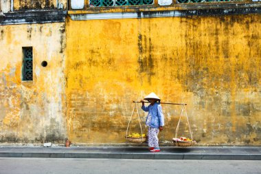 Hoi An, Quang Nam, Vietnam, 26 Nisan, 2018:Vietnamese kadın sokak satıcı Hoi antik kenti Hoi bir Vietnam'da bir tipik sarı evlerin manzaralı