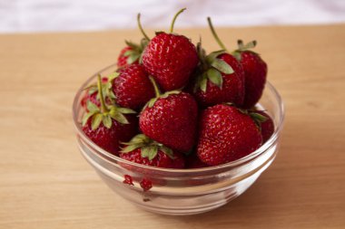 Yıpranmış beyaz bir arka plan üzerinde bir cam tabak yukarıdan çekilen güzel, olgun kırmızı çilek.